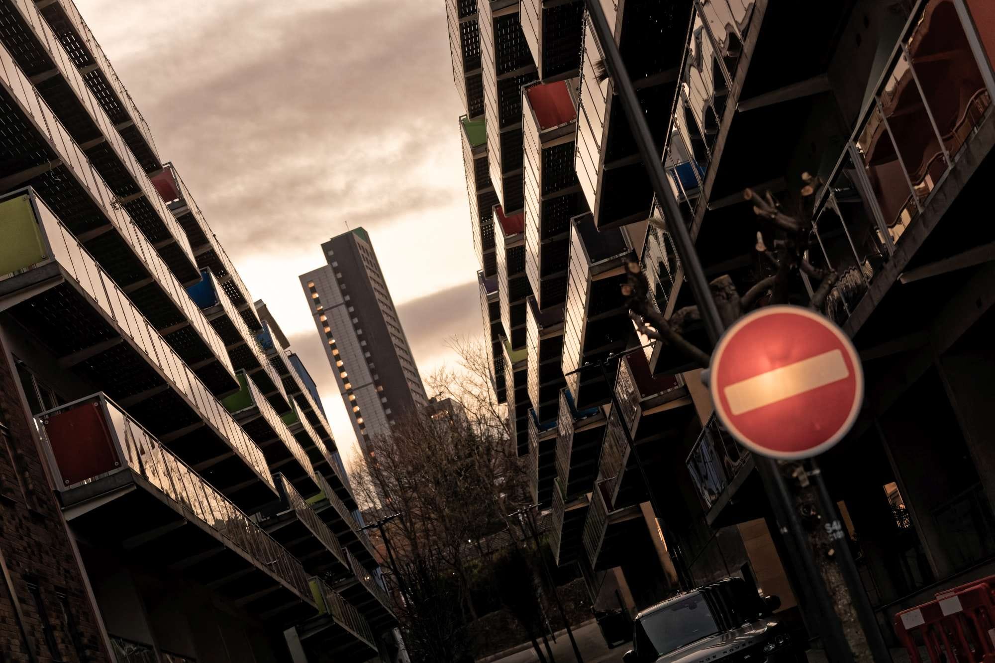 Tall buildings with colorful balconies line a narrow street at sunset, featuring a prominent "Do Not Enter" sign in the foreground.