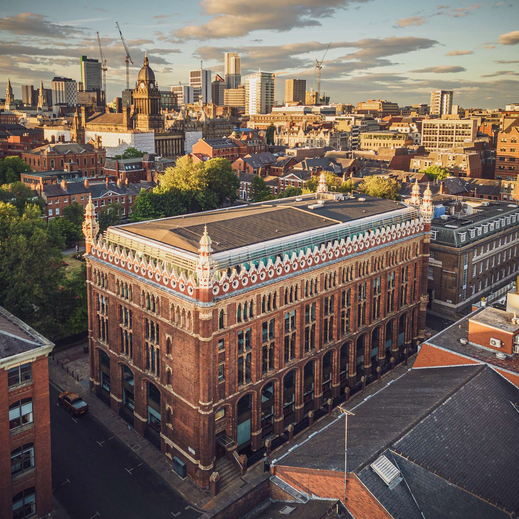 Aerial view of Leeds cityscape at sunset, featuring the historic red-brick Leeds Grand Theatre with modern buildings in the background.