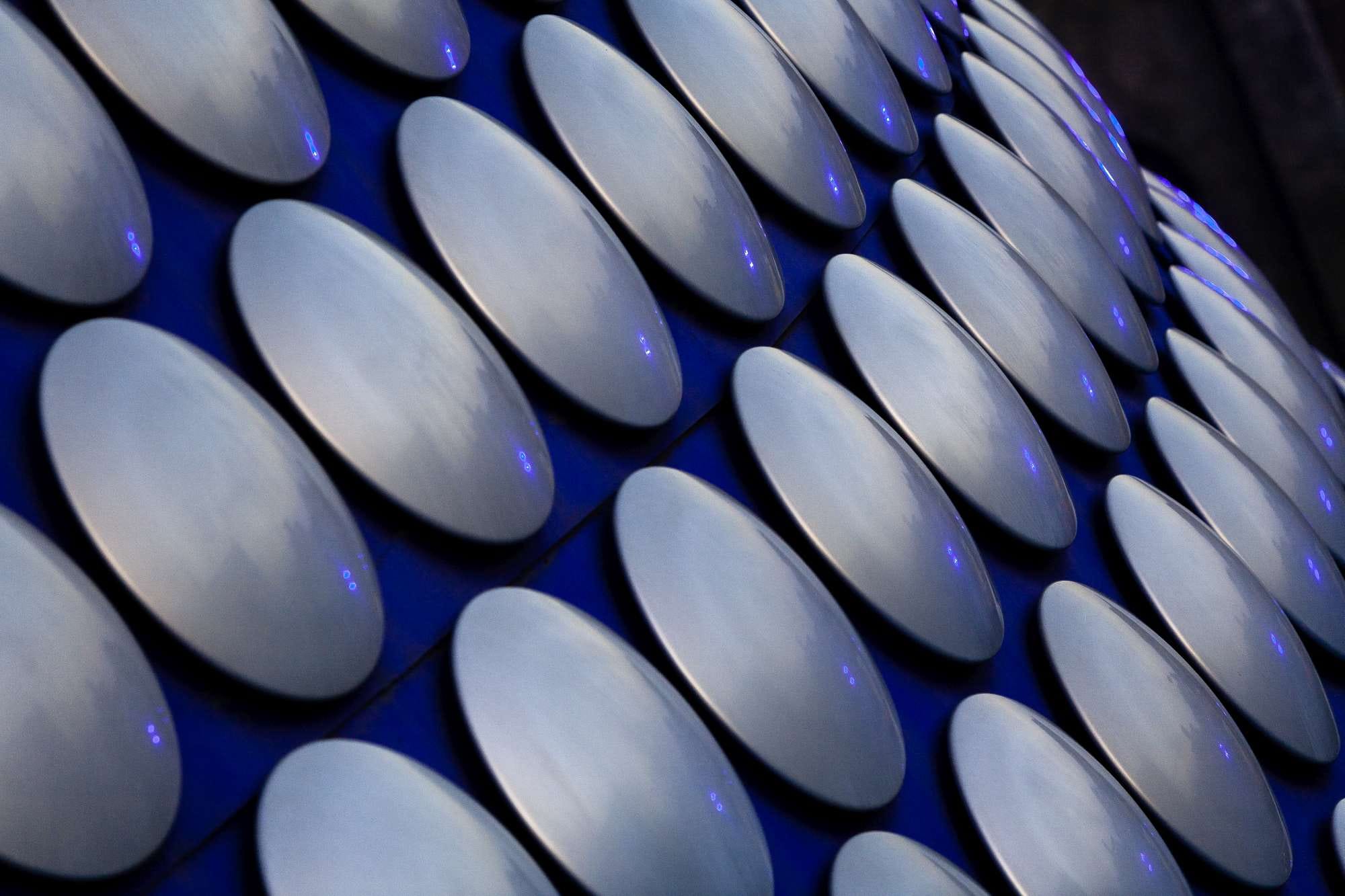 Close-up of a building facade with a pattern of large circular metallic discs reflecting blue light.