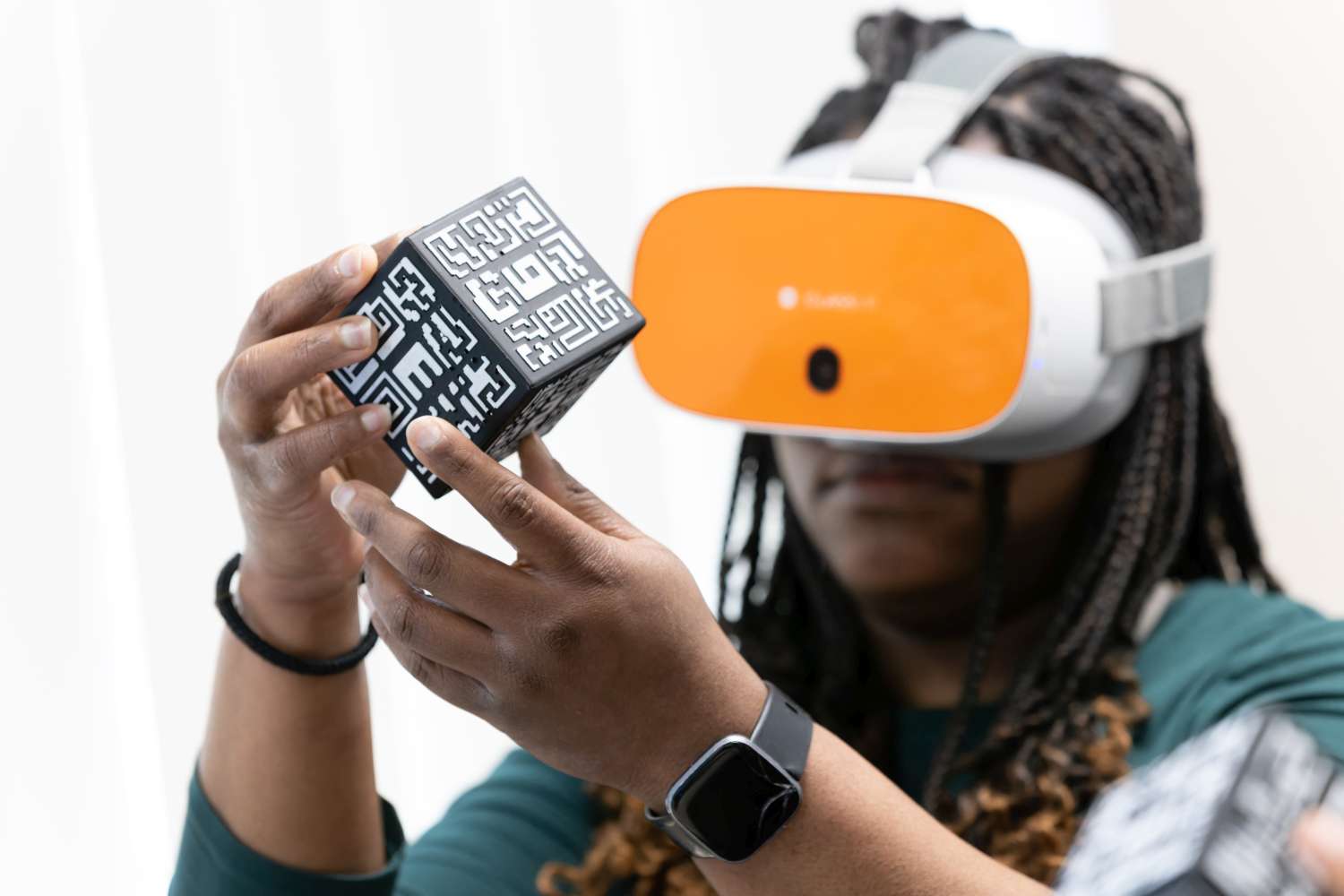 Person wearing an orange VR headset examines a black and white coded cube with both hands.