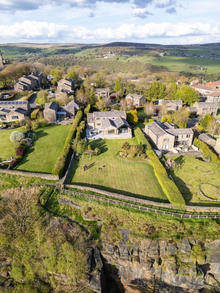 Aerial view of a peaceful village with stone houses, neatly trimmed gardens, and expansive green fields in a rural landscape.