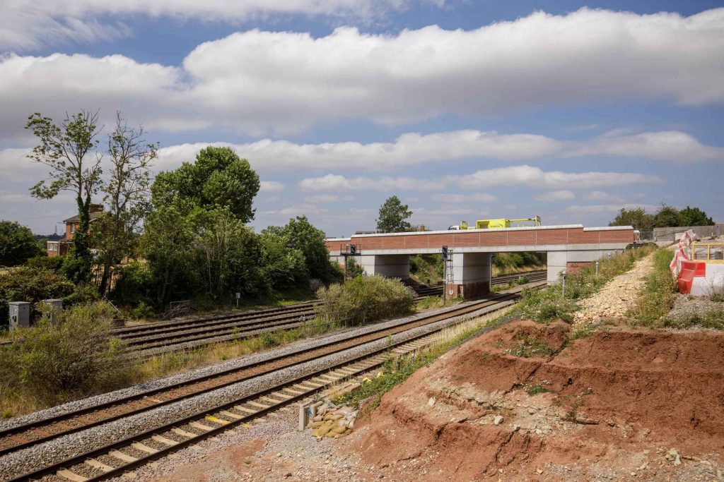 Wide view of an infrastructure bridge crossing over railway tracks, with excavated ground alongside