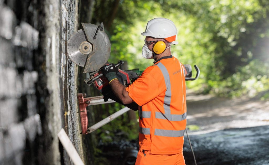 Worker in hi-vis and ear defenders operating a cutting tool on concrete pipe sections