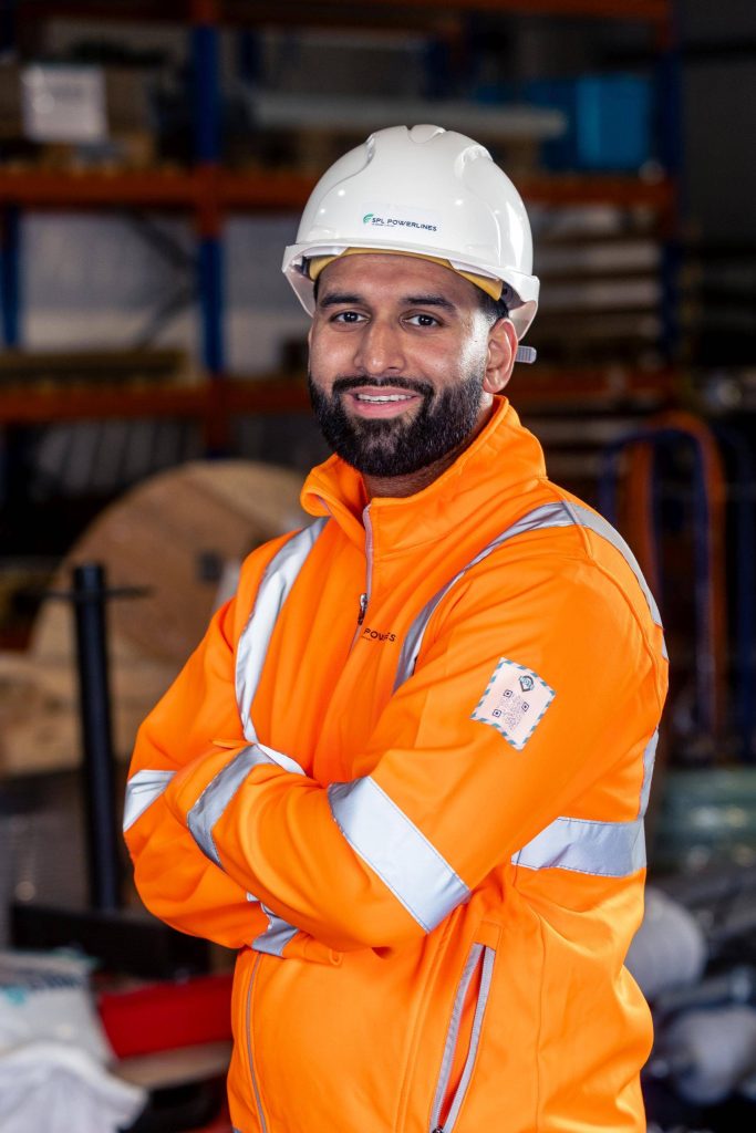 Portrait of a construction worker in orange hi-vis and a white hard hat, smiling, arms crossed