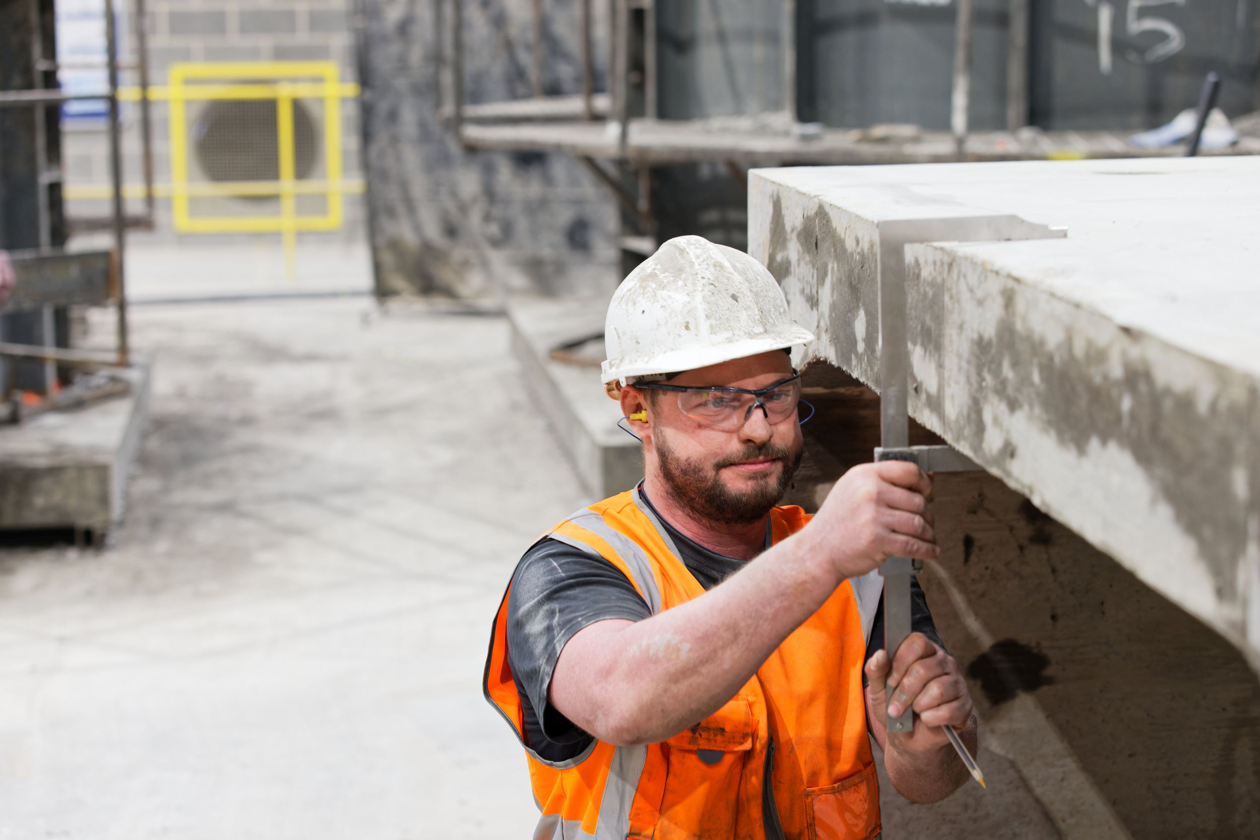 Site worker in a hard hat and hi-vis inspecting a precast concrete beam with a set square