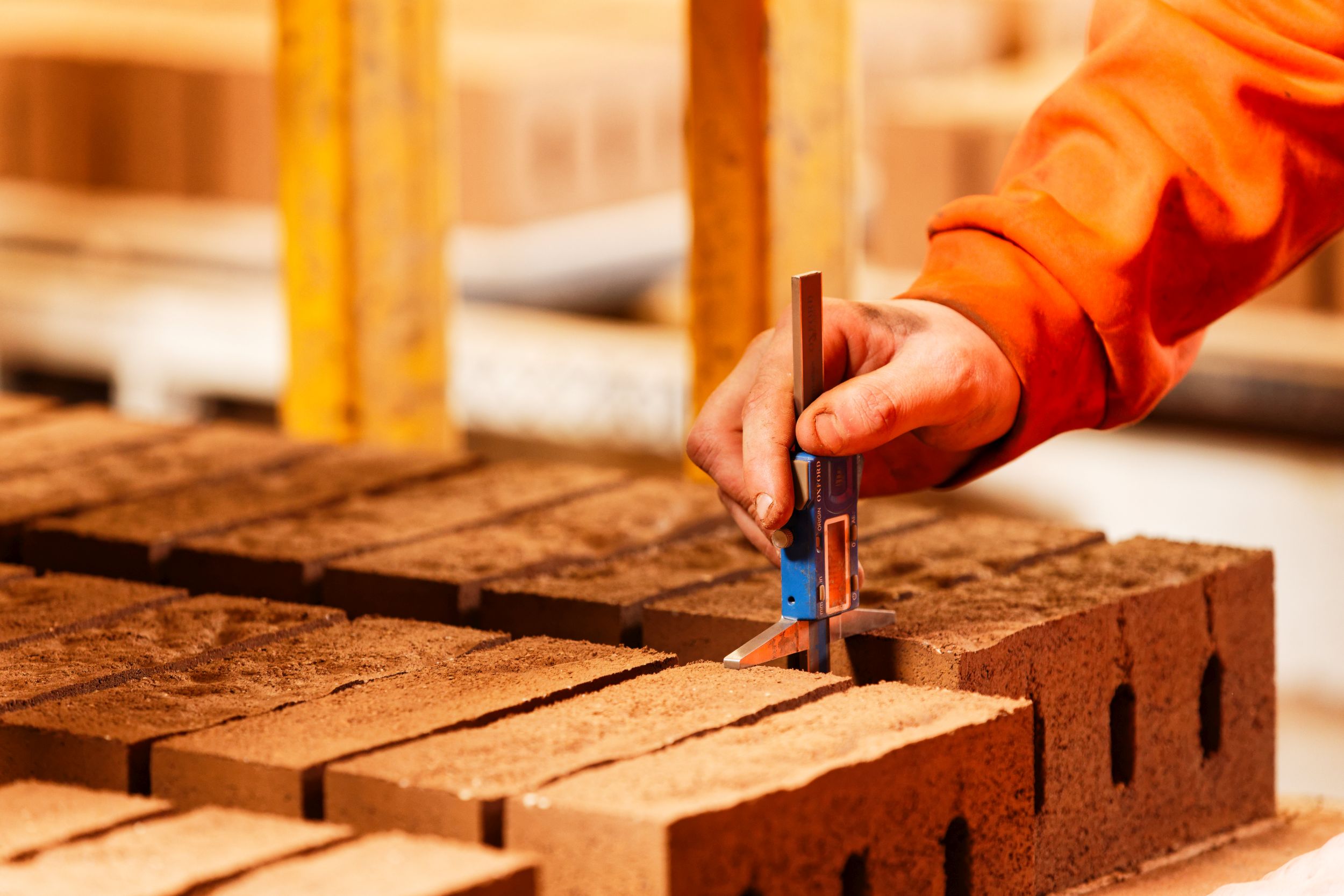 Close-up of a worker's hands using digital calipers to check the dimensions of a brick