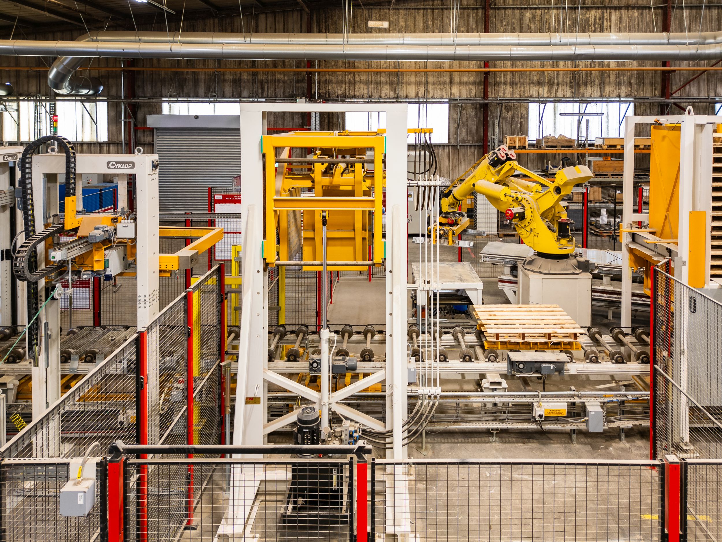 Yellow robotic arm and automated palletising machinery inside a manufacturing warehouse