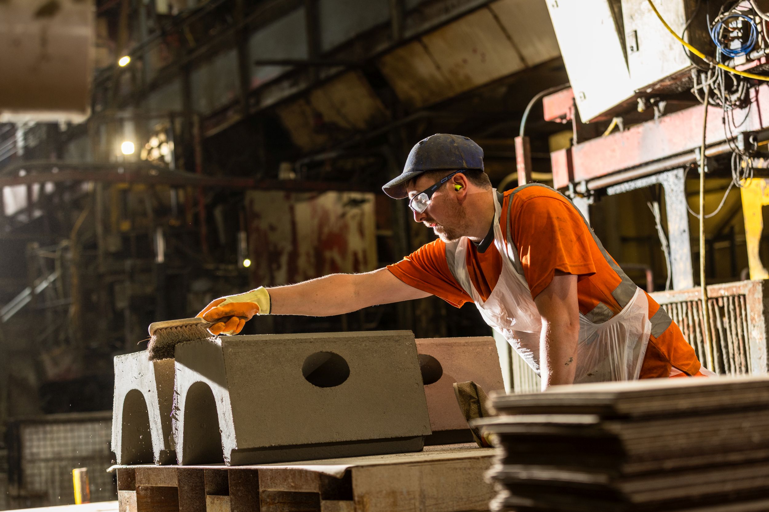 Worker in hi-vis brushing down a freshly cast concrete block on the production line