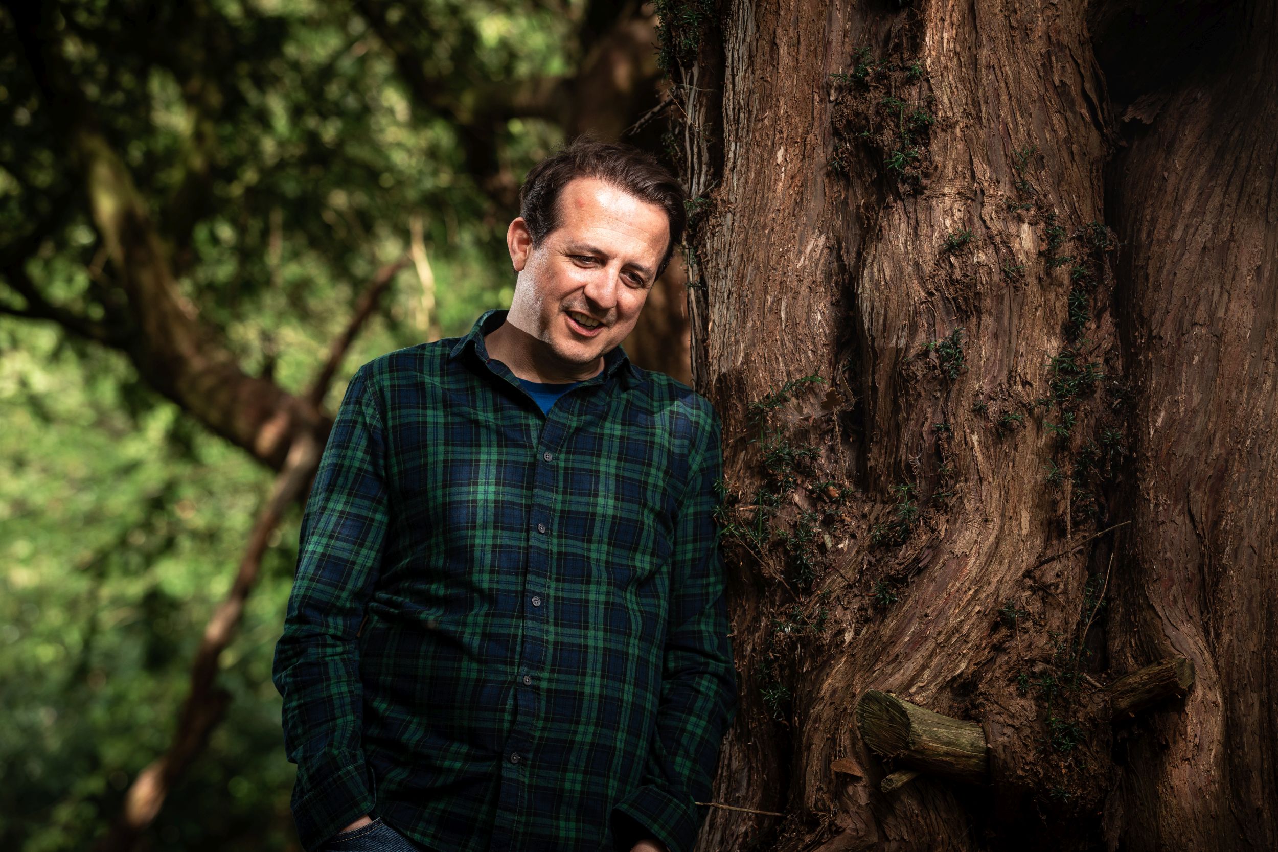 Smiling man leaning against a large tree trunk in woodland