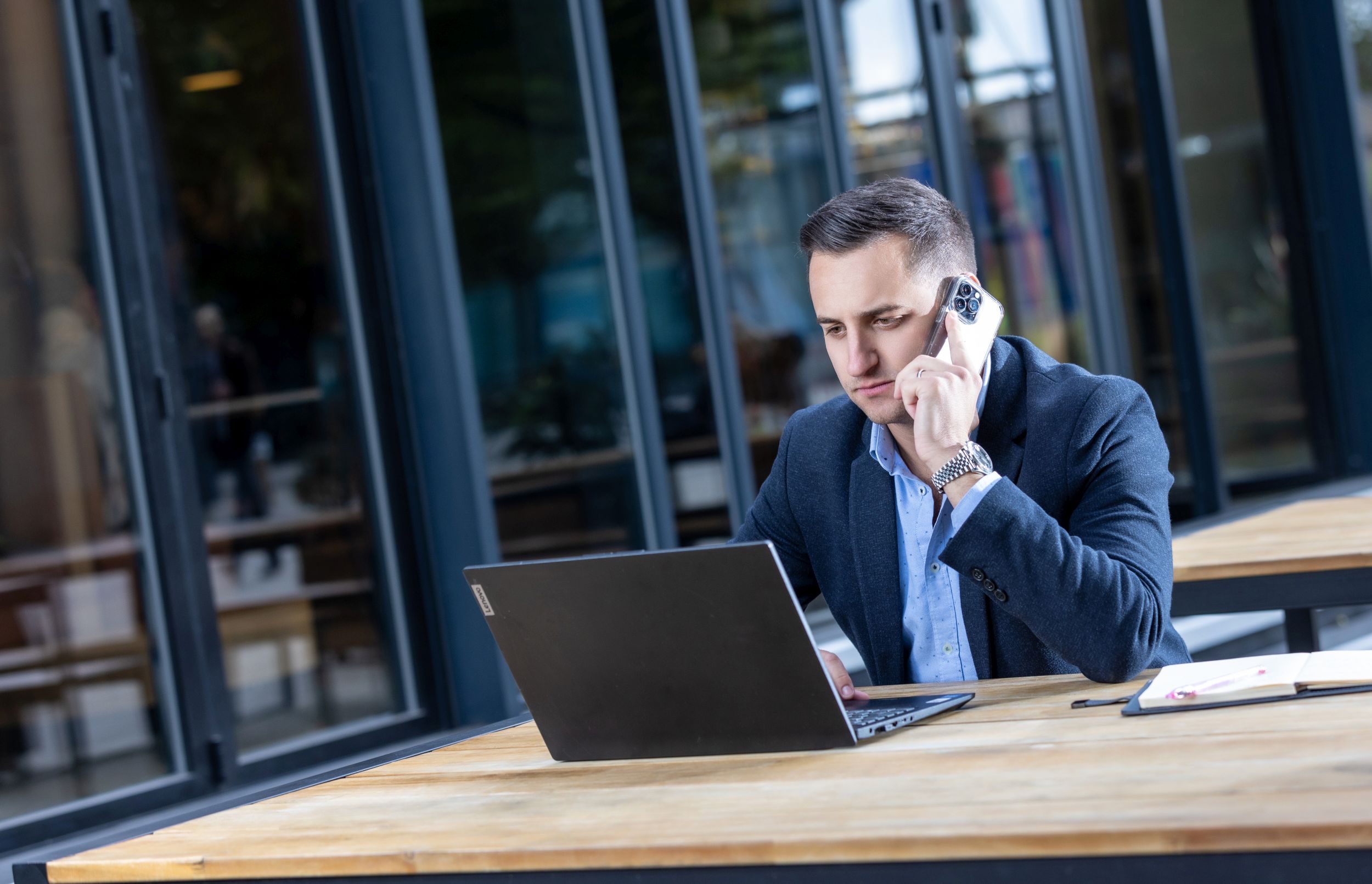 Man on the phone working at a laptop at an outdoor cafe table