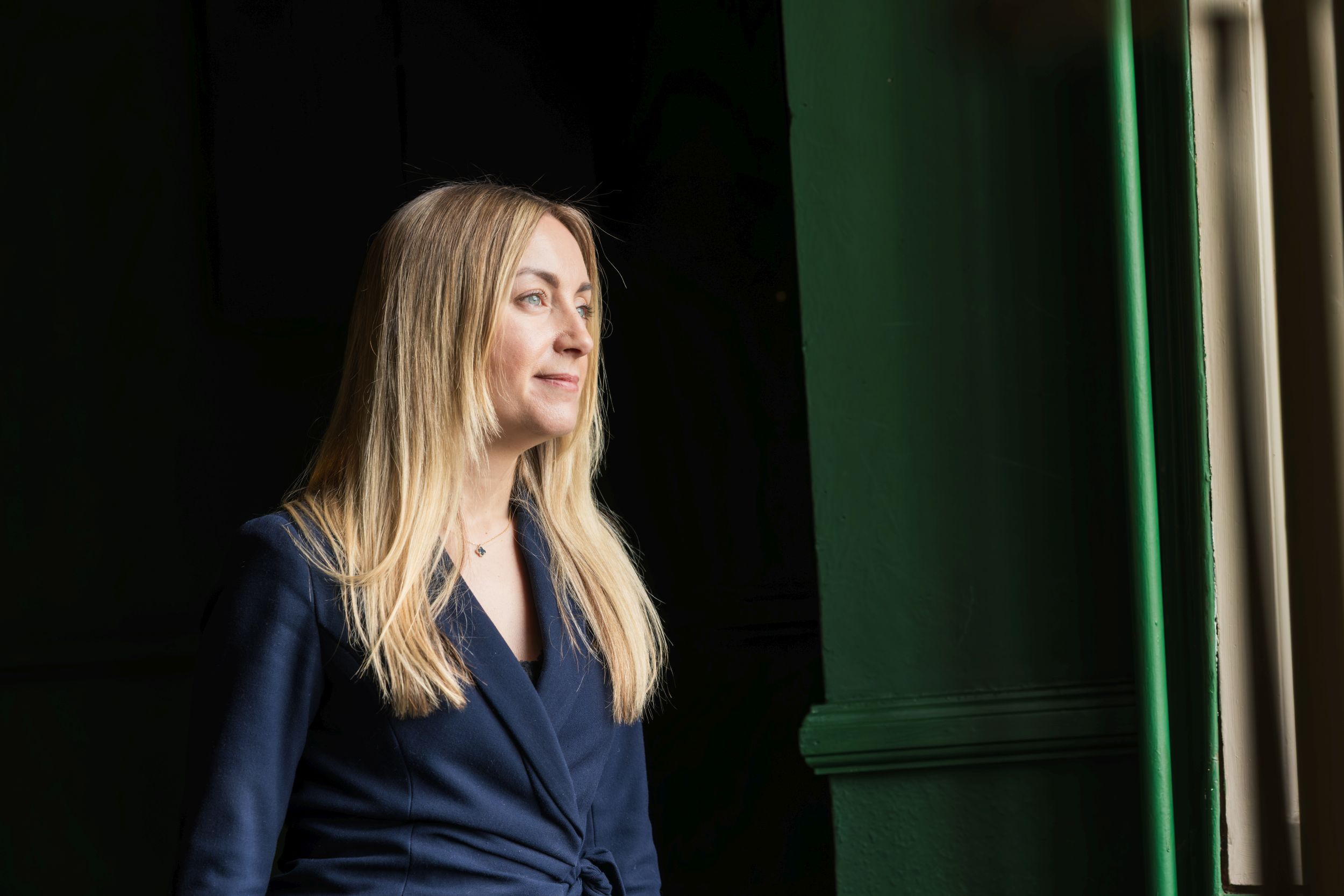 Woman in profile portrait, dramatic window light against a dark green backdrop
